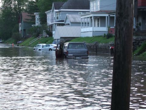 1989 Ford Bronco - A dark SUV and other vehicles are submerged in floodwaters on a residential street.