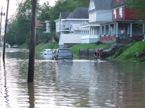 1989 Ford Bronco - A street is flooded, with a dark SUV and a white car partially submerged in the water.