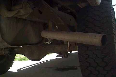 Underside view of a vehicle's rear axle and exhaust pipe. Tire visible on the right
