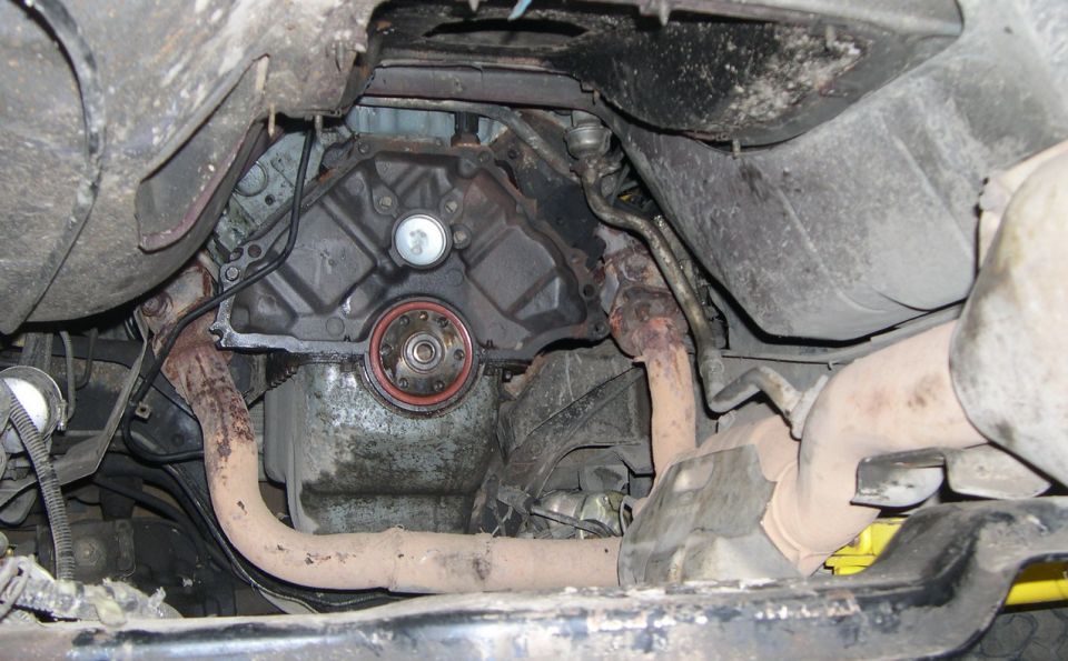 Underside view of a vehicle's engine and exhaust system, showing a transmission seal and rusty pipes