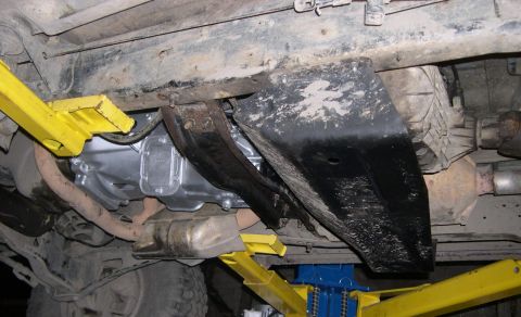1989 Ford Bronco - The underside of a vehicle shows a recently installed transmission and protective skid plate, likely part of a modification or upgrade.