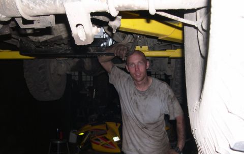 1989 Ford Bronco - A mechanic poses for a photo while working on the underside of a vehicle, which is raised on a lift.