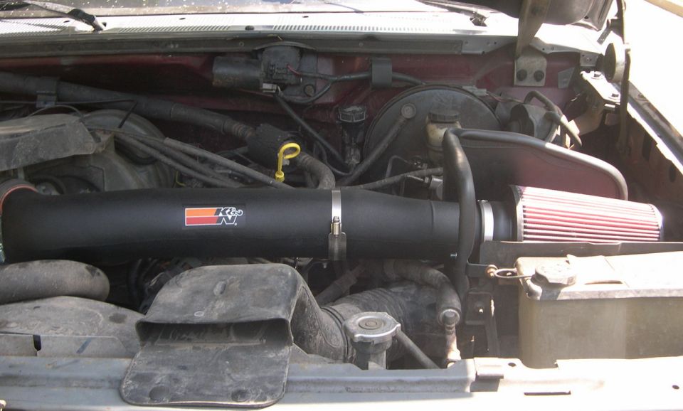 Engine bay with black K&N air intake system and red filter. Maroon paint visible