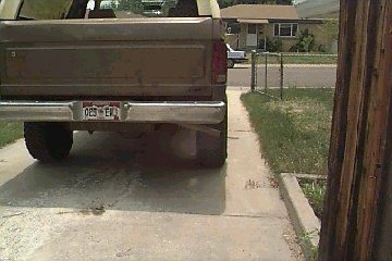 1980 Ford Bronco - This image shows the rear end of a pickup truck, with a visible license plate and a portion of a house in the background.
