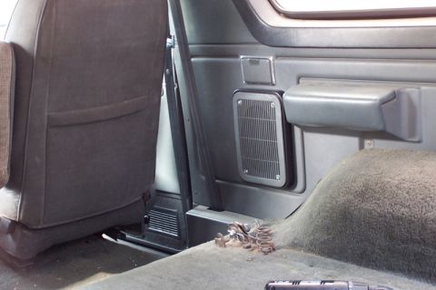 1990 Ford Bronco - The interior of a vehicle shows a speaker grille mounted on the side panel, with a dark gray seat visible.