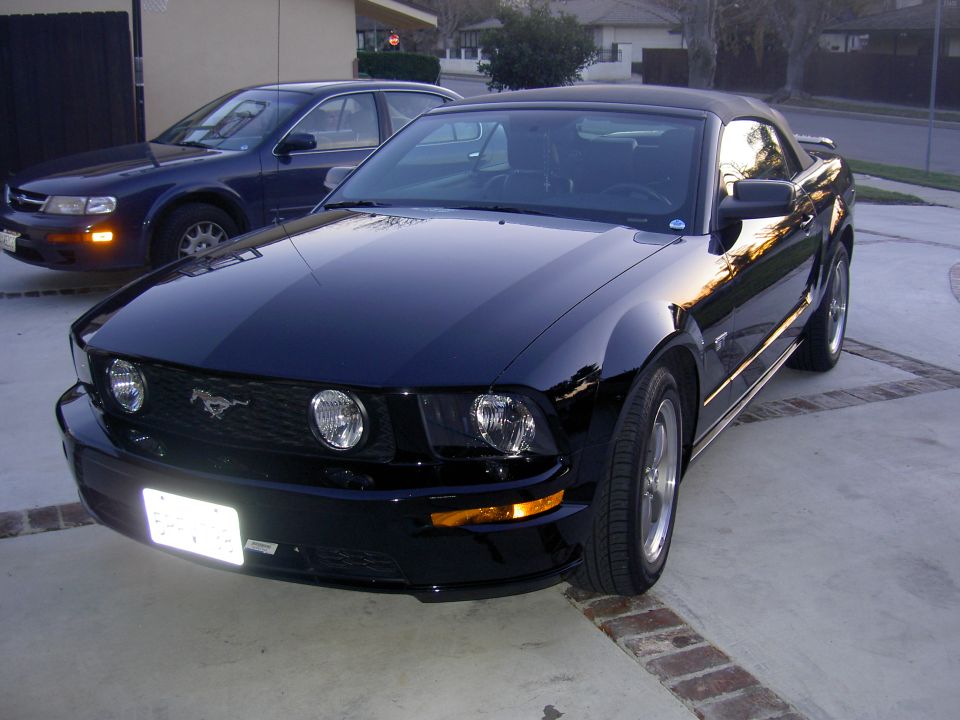 Black Ford Mustang convertible with racing stripes, parked on a driveway