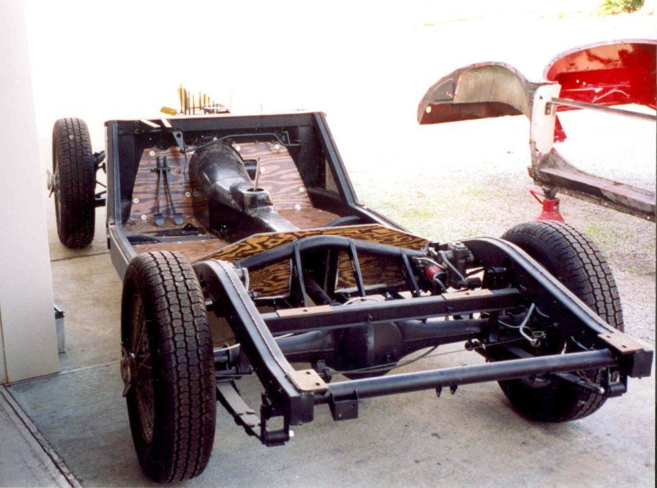 Restored black car chassis with wood floorboards and wire wheels in a garage