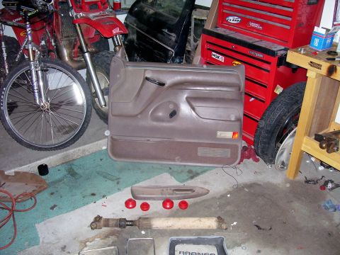 1991 Ford Bronco - A brown Ford Bronco door panel is displayed on a garage floor alongside other vehicle parts and tools.
