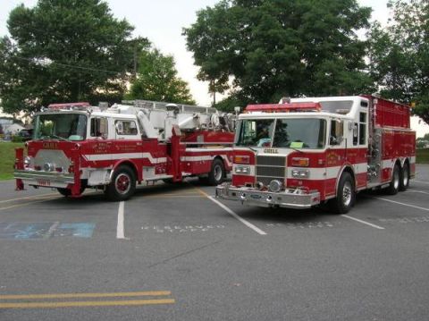 1989 Ford Bronco - Two fire trucks are parked in a lot, one equipped with a ladder, under a cloudy sky.