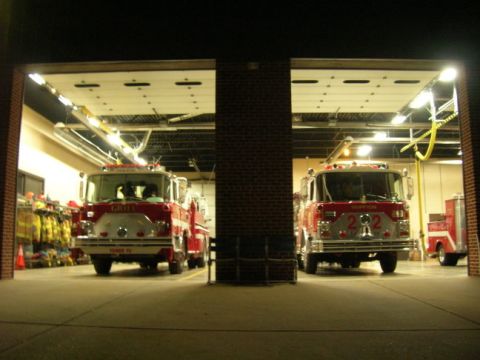 1989 Ford Bronco - Two fire trucks are parked side-by-side in a fire station, with their garage doors open.