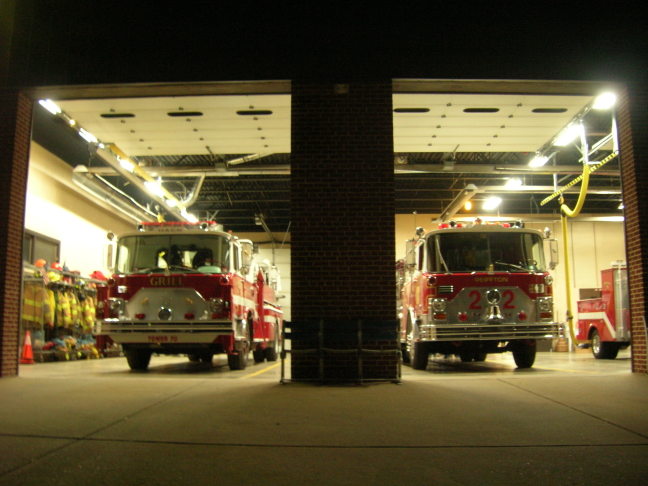 Two red fire trucks parked inside a fire station garage at night