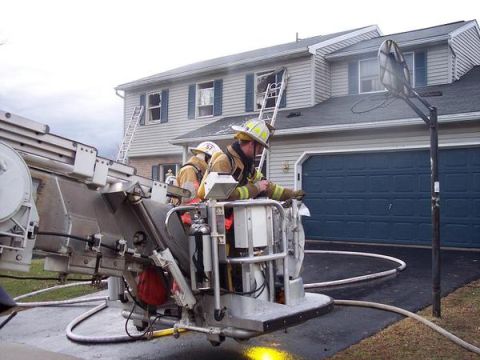 1989 Ford Bronco - Firefighters are positioned on a ladder truck outside a house, with a ladder extended to an upper window.