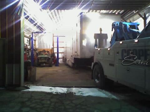 1992 Ford Bronco - A tow truck and trailer are parked inside a garage, with a small vehicle visible in the background.