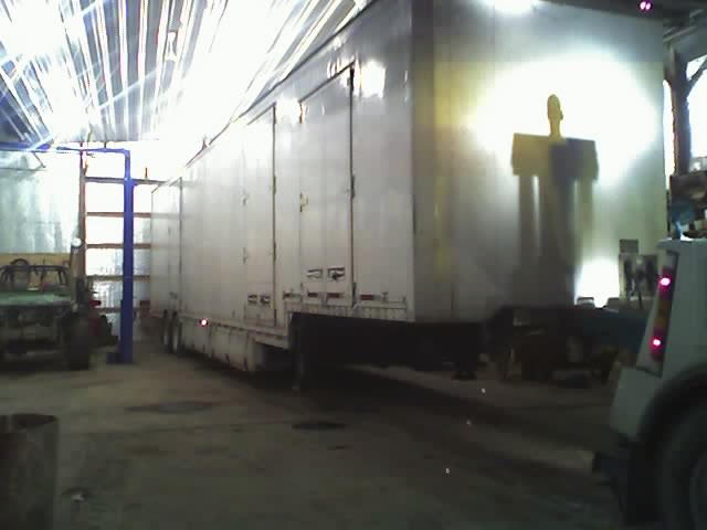 Large white trailer in a workshop with a partial truck visible on the right