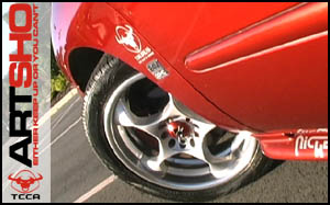 1998 Ford Taurus - Detail shot of a red car's wheel and fender, showing various decals and the alloy rim.