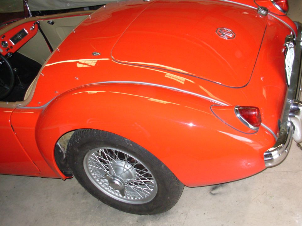 Orange MG A roadster rear quarter with wire wheel, chrome bumper and MG badge in a garage
