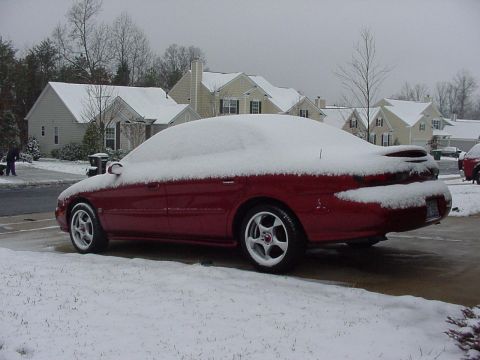 1998 Ford Taurus - A red sedan is parked outside a house, completely covered in snow.