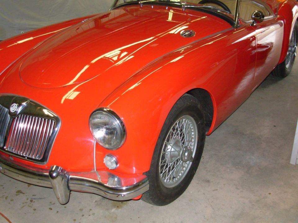 Red MGA roadster front three-quarter view with chrome grille, MG badge, and wire wheels indoors