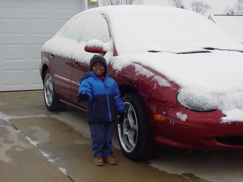 1998 Ford Taurus - A child stands next to a snow-covered 1998 Ford Taurus in front of a garage.