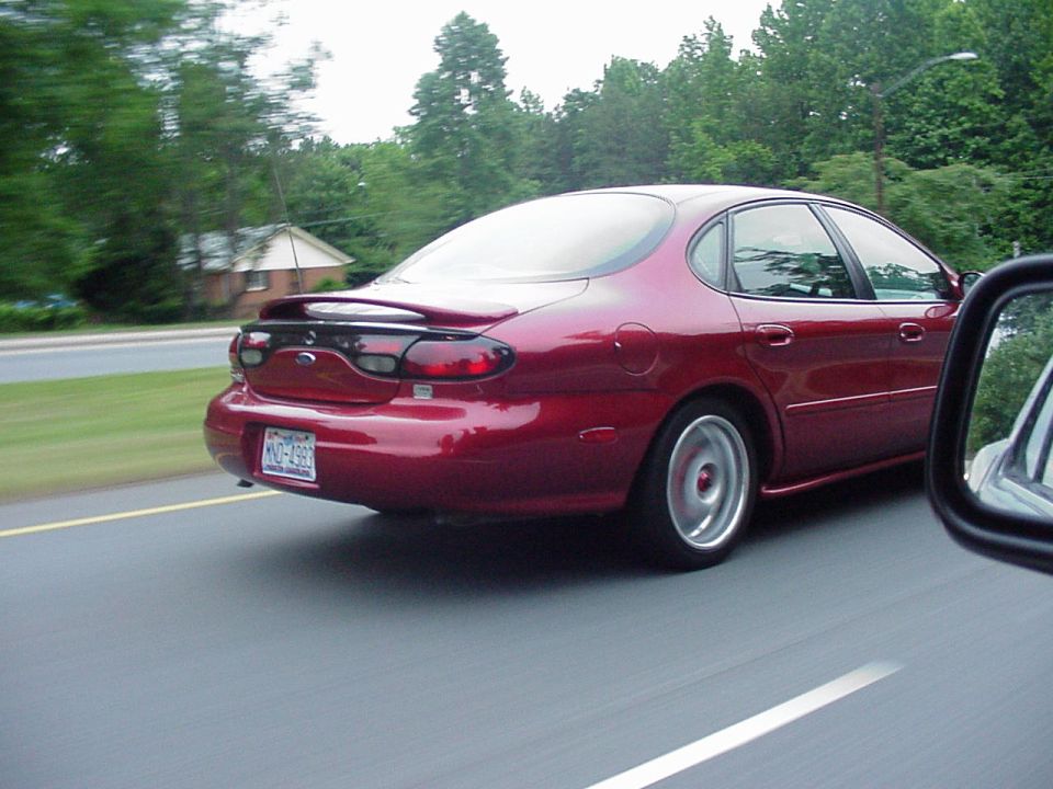 Red 1998 Ford Taurus rear view driving on a road