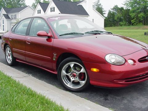 1998 Ford Taurus - A red 1998 Ford Taurus sedan is parked on the side of the road with houses in the background.