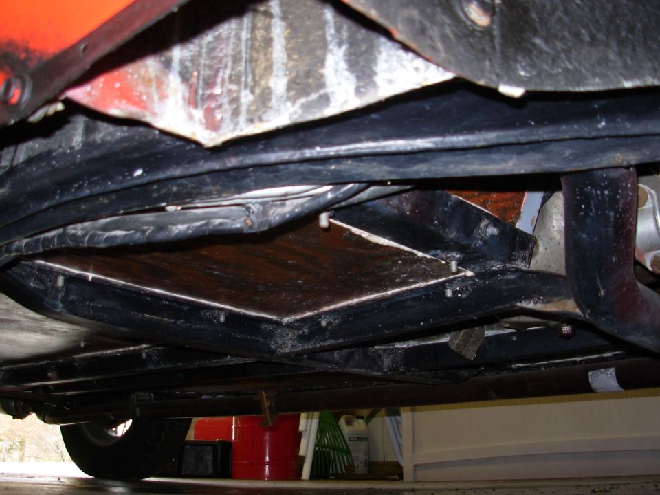 Underside view of a car's frame and floor pan, showing some rust and repairs