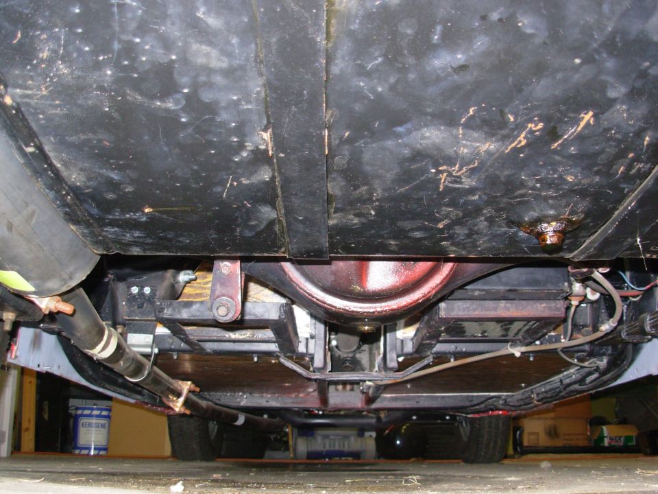 Underside view of a car's rear axle, exhaust, and fuel tank. Shows suspension components and underbody