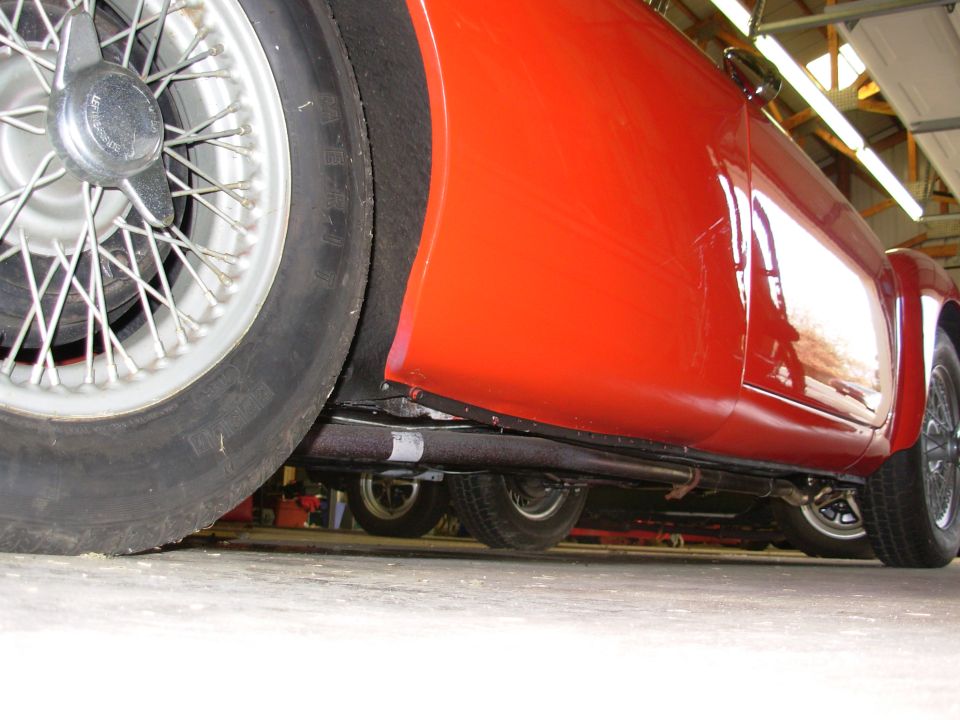 Low angle shot of a red sports car's side and undercarriage, showing wire wheels and exhaust