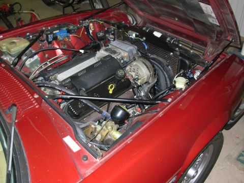1992 Jaguar XJ-S - The engine bay of a red car is open, revealing a V8 engine with a Corvette-branded valve cover and various hoses and components.