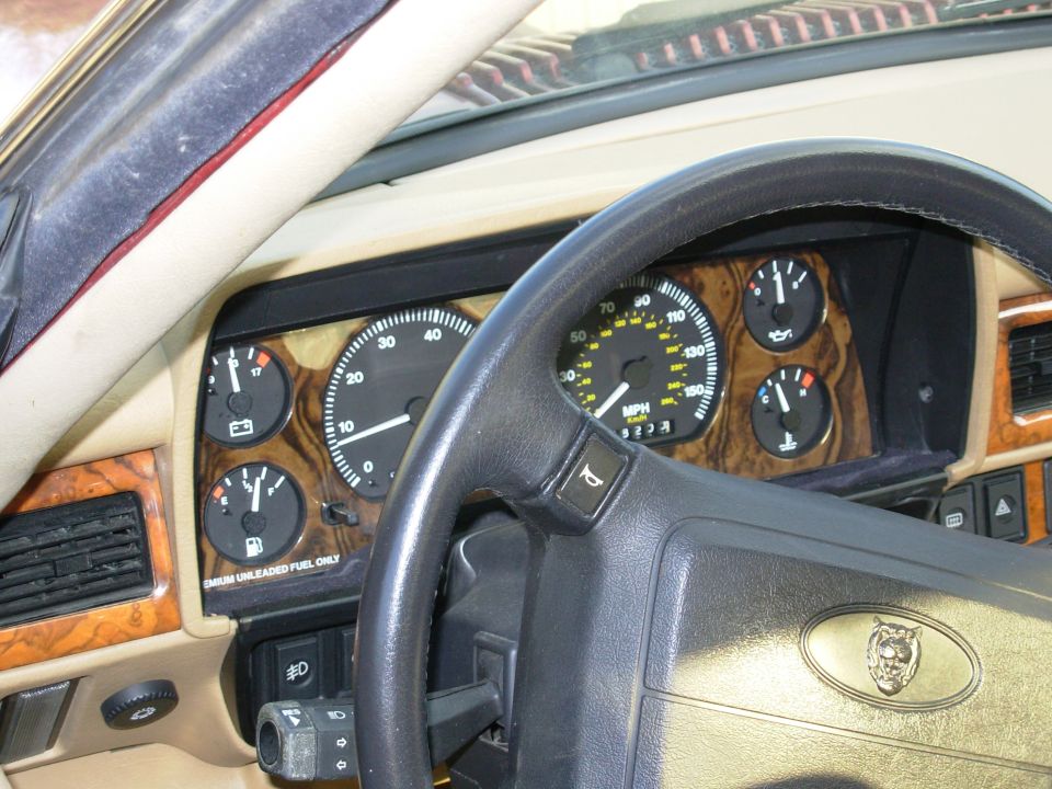 Jaguar interior showing burl wood instrument cluster, gauges, and black steering wheel with Jaguar emblem