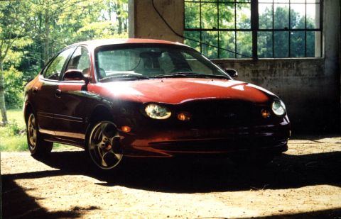 1998 Ford Taurus - A red 1998 Ford Taurus is parked outdoors in front of a building with large windows.