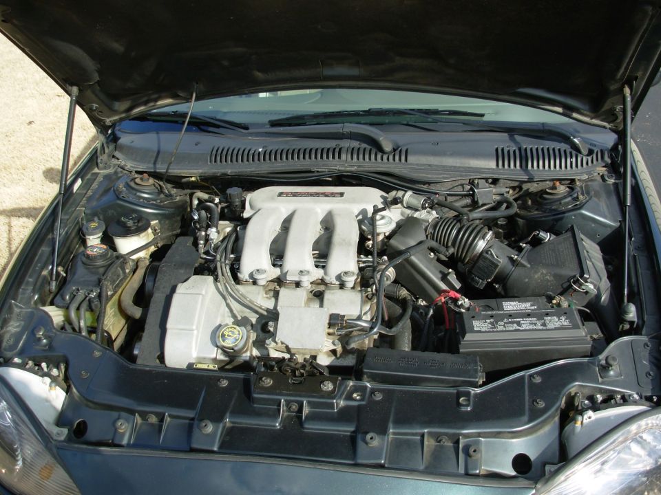 Car engine bay with V6 engine, air intake, and battery visible
