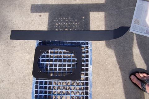 1990 Ford Bronco - Speaker adapter and a black trim piece are laid out on a grate outdoors.