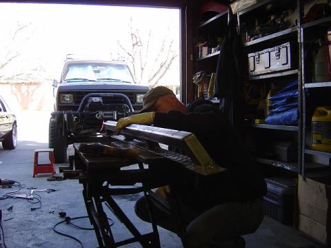 1986 Ford Bronco II - Man works on metal fabrication in a garage, with a 1986 Ford Bronco II visible in the background.