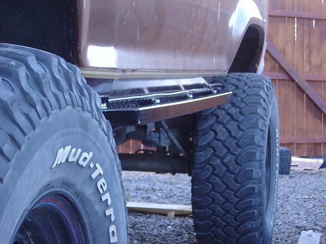 Side view of a brown SUV with large off-road tires and a step bar