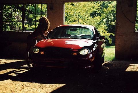 1998 Ford Taurus - A red 1998 Ford Taurus is seen from the front in a garage with a woman leaning on its hood.