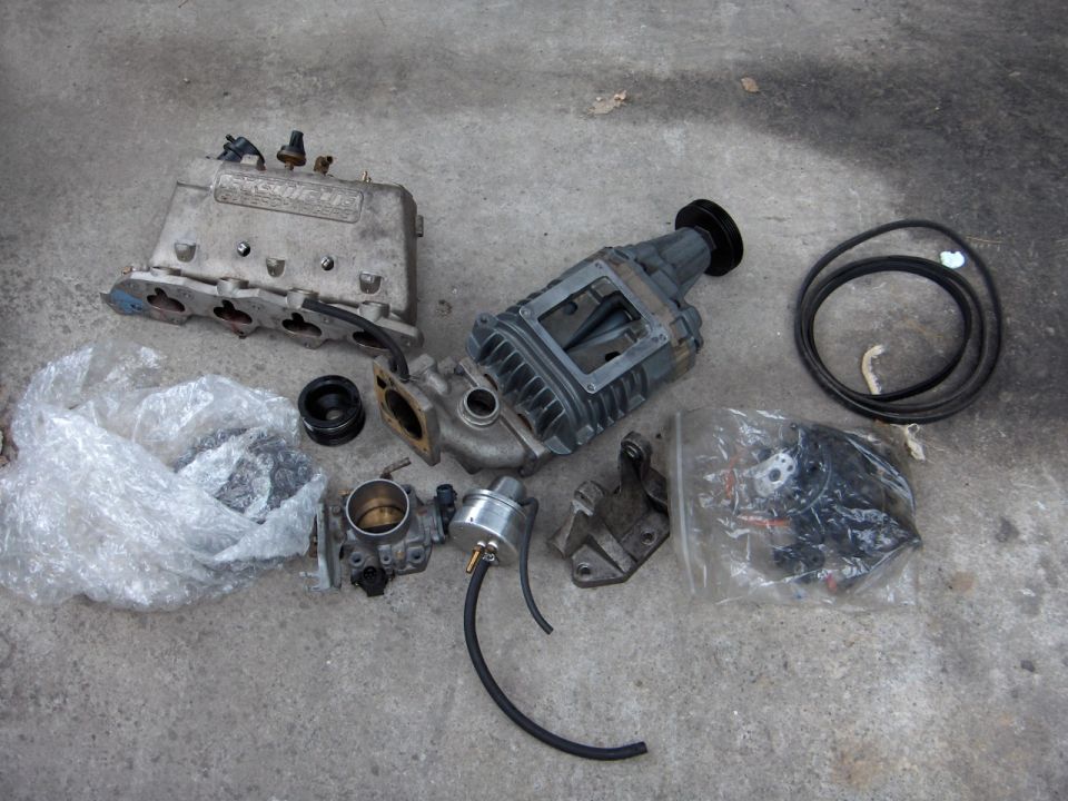 Supercharger kit parts, manifold, throttle body and belt on concrete floor
