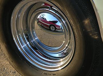 1976 Ford Thunderbird - A reflection in the chrome wheel shows a red car with its hood open, parked on a street.