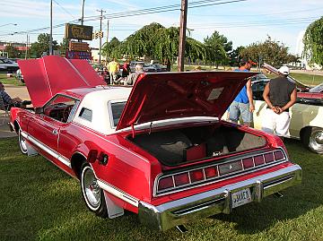 1976 Ford Thunderbird - A red and white coupe with its trunk and hood open, parked on grass with other vehicles nearby.