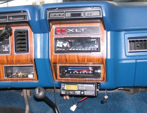 1984 Ford Bronco - The interior of a 1984 Ford Bronco features wood grain trim, an XLT badge, and an aftermarket radio and CB unit.