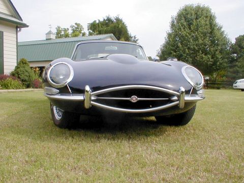 1967 Jaguar XKE - A dark blue 1967 Jaguar XKE convertible is parked on a grassy lawn in front of a building.