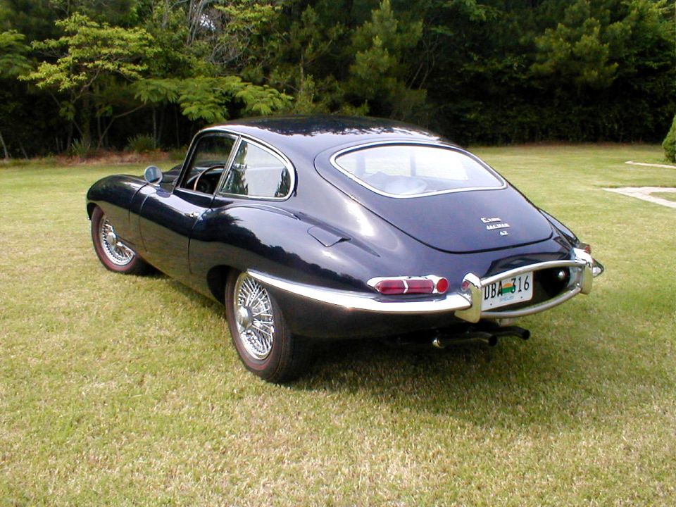 Dark blue Jaguar E-Type coupe rear three-quarter view on a lawn with wire wheels