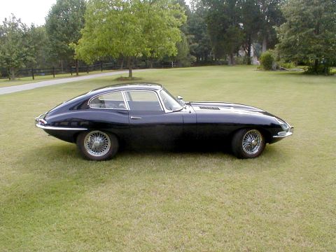 1967 Jaguar XKE - A classic black Jaguar E-Type coupe sits on a grassy lawn with trees in the background.