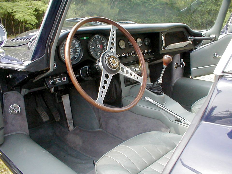 Classic Jaguar interior with wood steering wheel, round gauges, and gray leather seats