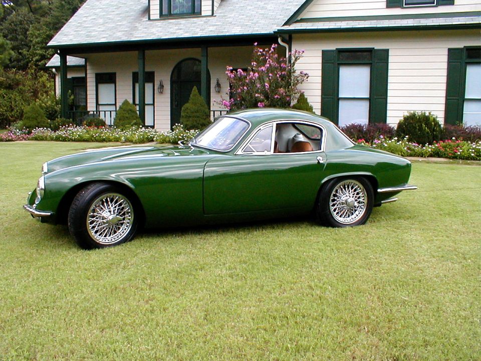Green vintage coupe with chrome wire wheels, side view on lawn by white house