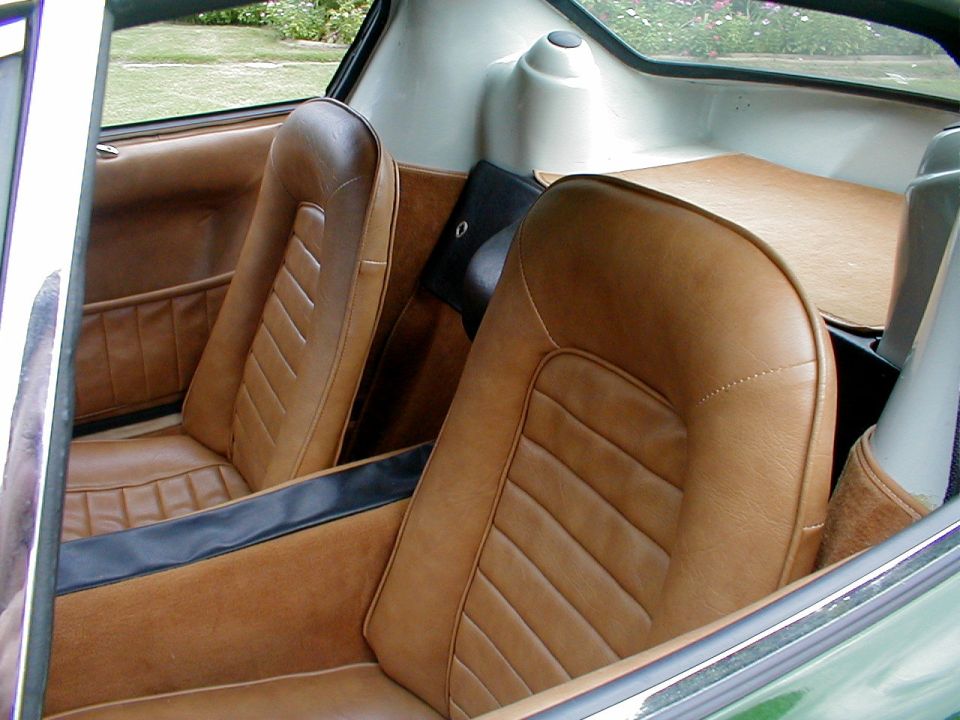 Tan leather bucket seats inside a small green sports car with garden visible