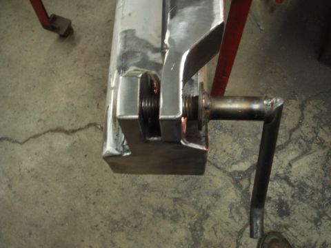 1996 Ford Bronco - Close-up of a metal clamp mechanism with a threaded rod and a crank handle, resting on a concrete surface.