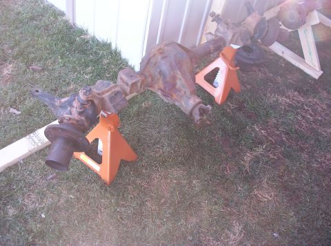 1987 Jeep Cherokee - Front axle assembly, likely for a Jeep, is supported by jack stands on a grassy area.