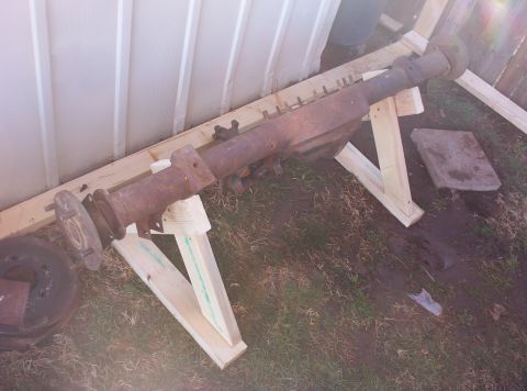 1987 Jeep Cherokee - A rusty vehicle axle is supported by wooden stands outdoors.