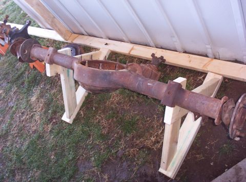 1987 Jeep Cherokee - A rusty rear axle assembly is supported by wooden stands on a grassy area.